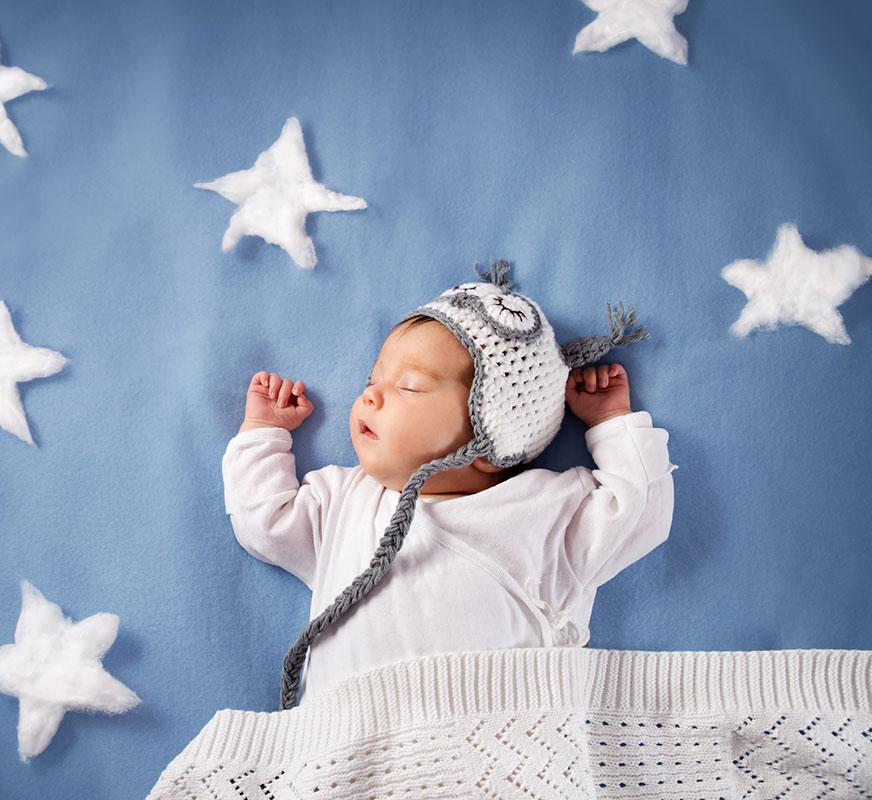 Cute newborn baby girl lying in the bed. 2 month old child in owl hat sleeping on blue blanket